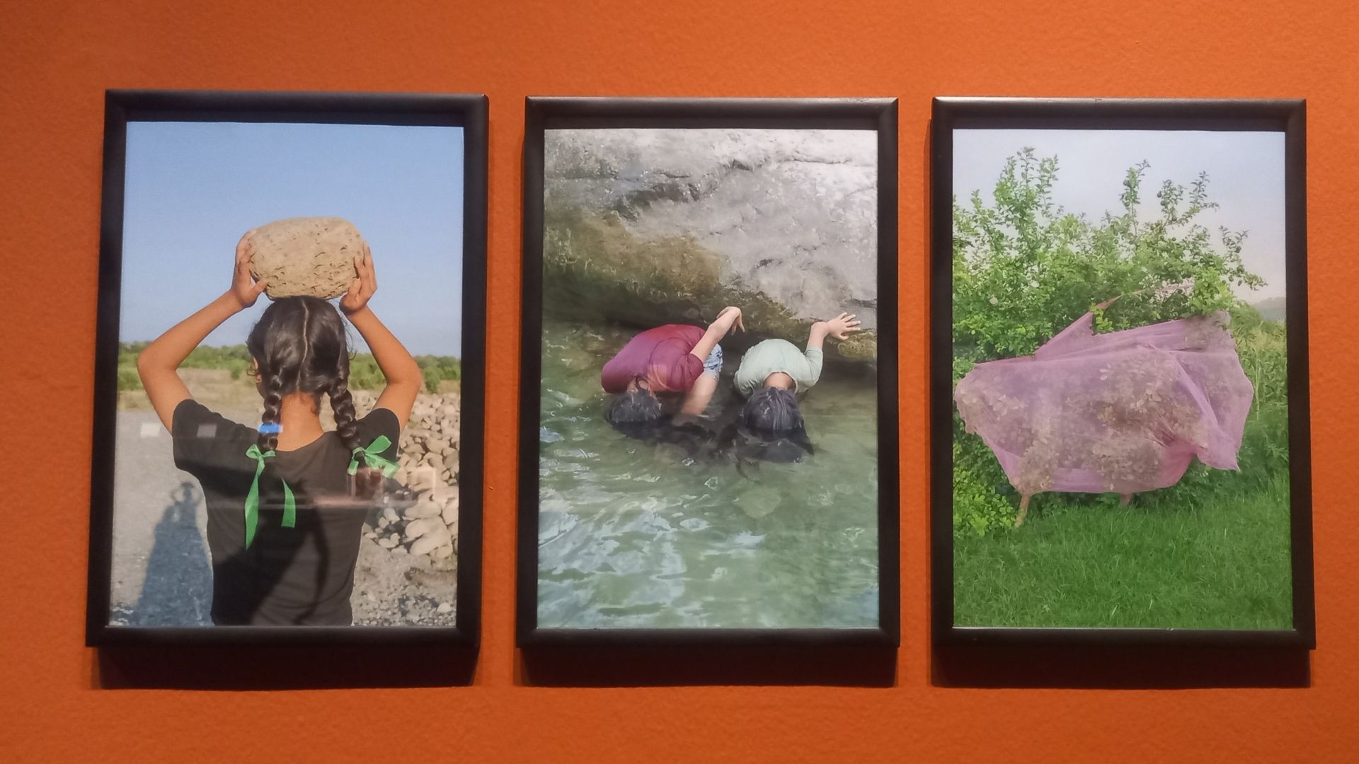Young girls dipping their hair in the river and a girl carrying stone showing artist’s memory of her village